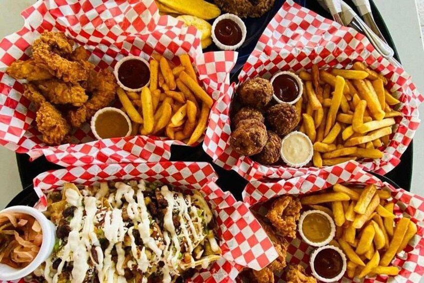 A tray with various fried foods including chicken, French fries, and meatballs, along with dipping sauces. 3