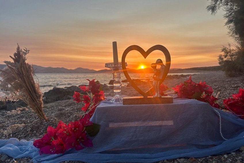 A sunset over a beach with a heart-shaped decoration, flowers, and a clear sky. 5