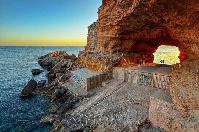 A coastal cave entrance with a staircase leading down to a platform. 1