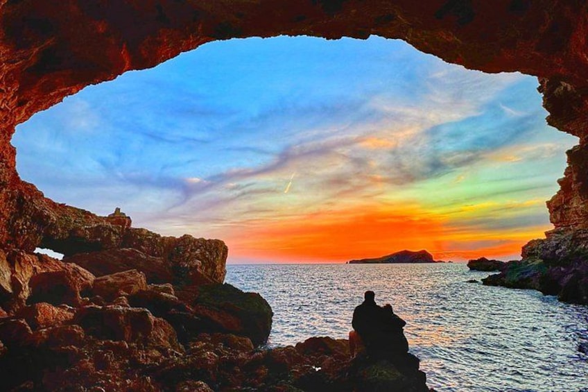 A coastal scene through a cave opening with a sunset, rocky formations, and calm sea. 5