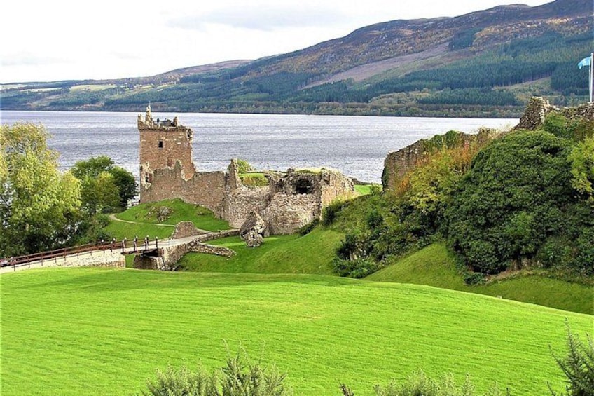 Ruinas de un castillo histórico junto a un lago, con campos verdes y colinas al fondo. 1