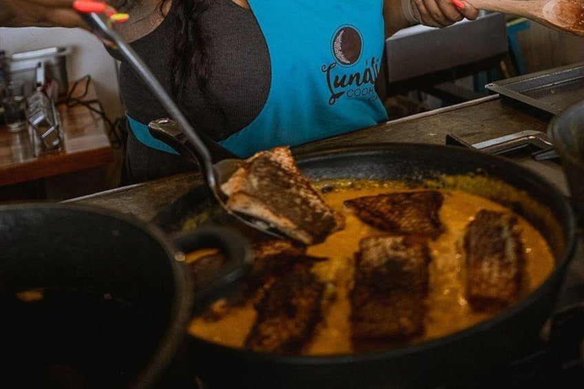 Una persona cocina en una cocina, usando un delantal azul con la palabra 'Lunati' escrita. 2