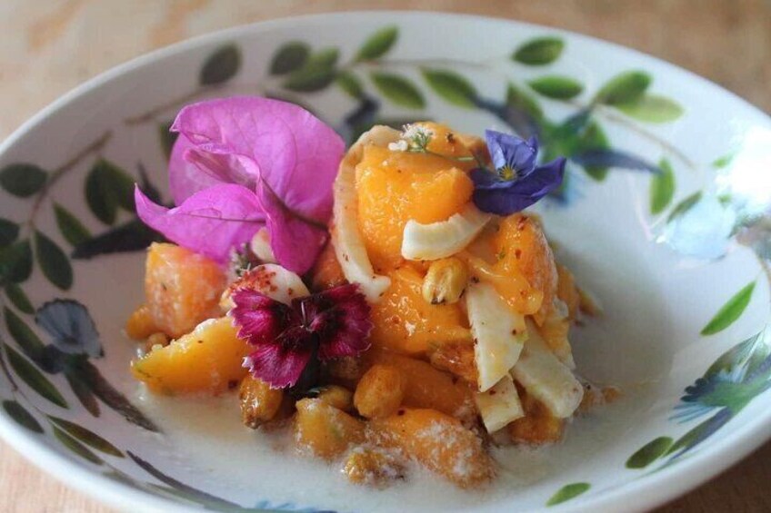 A plate of food with orange chunks, nuts, and purple flowers. 2