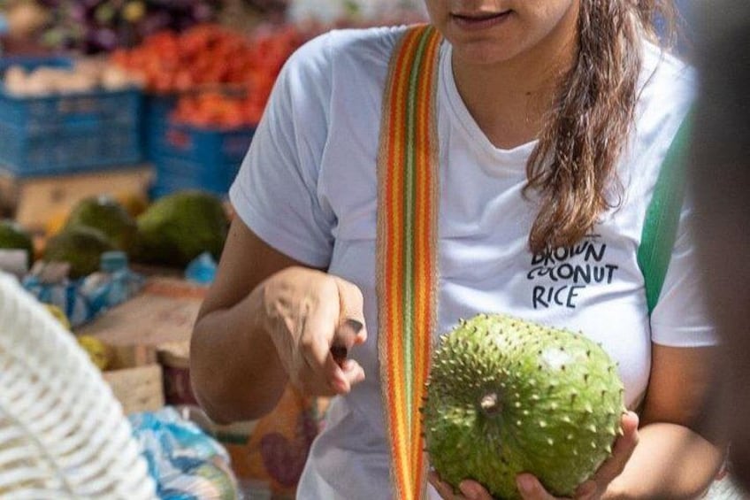 Una persona sosteniendo una fruta verde en un mercado. 3