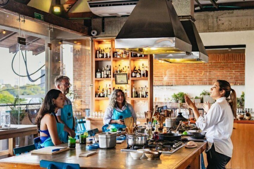 A group of people in a kitchen with cooking utensils, a brick wall, and a window overlooking greenery. 5