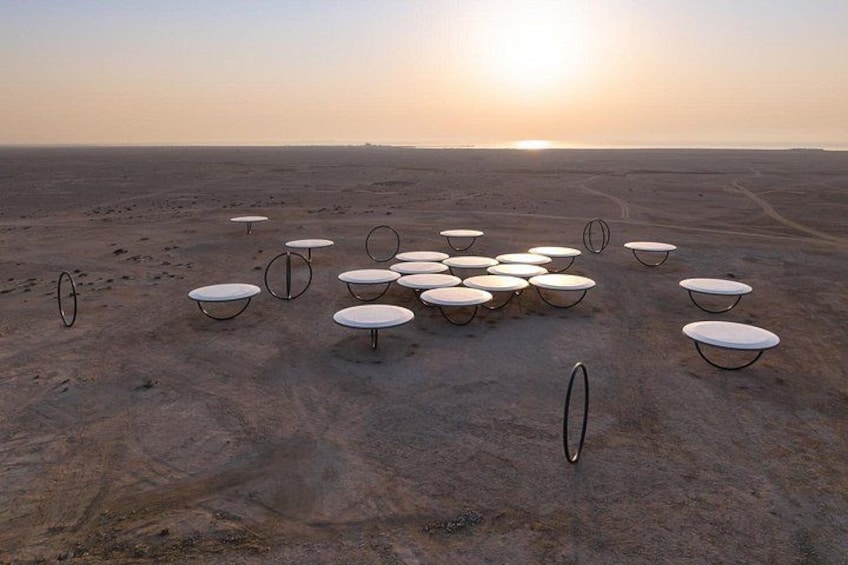 A desert landscape with multiple white tables and chairs arranged in a circle. 1