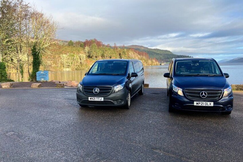 Two Mercedes-Benz vans parked on a wet road with a lake and trees in the background. 5