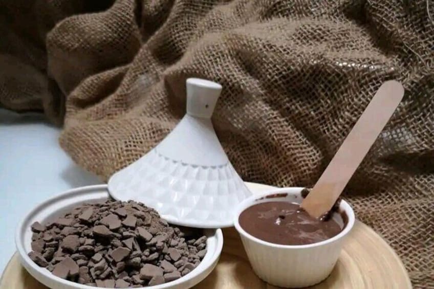 A bowl of chocolate pieces, a white container with a spoon, and a wooden surface. 3