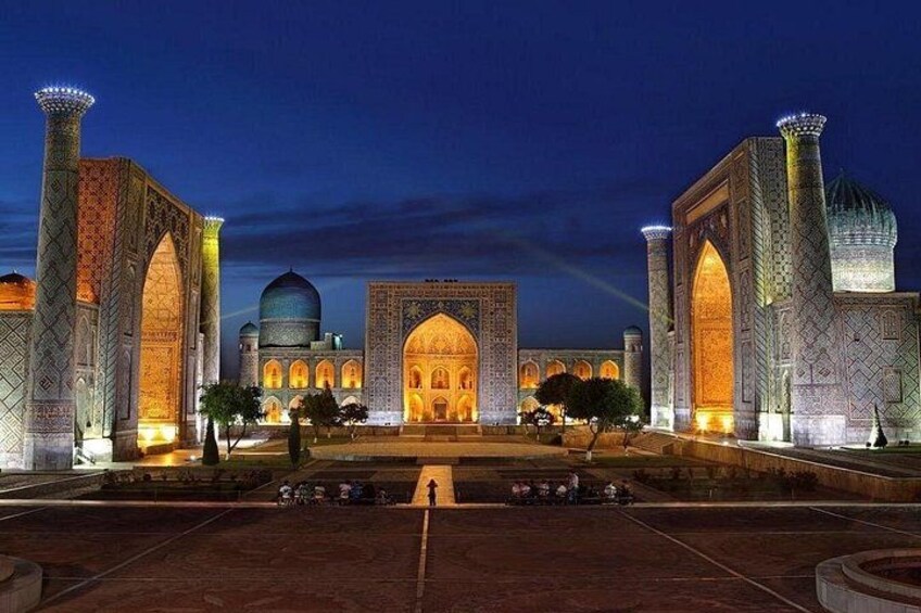 A large, illuminated building with domes and arches, surrounded by a paved area. 1