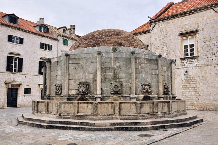 A historical stone fountain with a dome, surrounded by old buildings with red-tiled roofs. 4