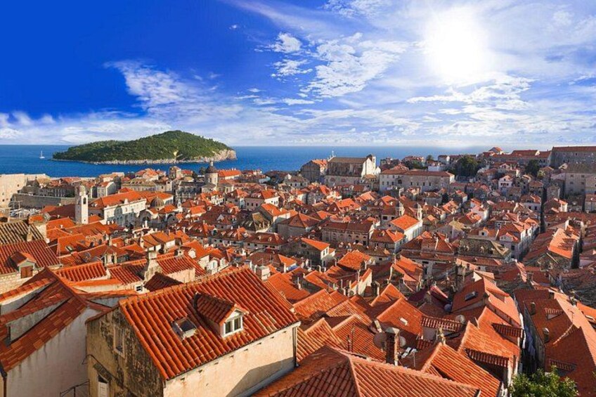 A coastal cityscape with red-roofed buildings, a prominent church, and a small island in the background. 5