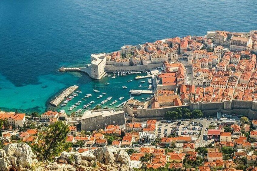 A coastal city with a historic fort, a harbor with boats, and red-roofed buildings. 1