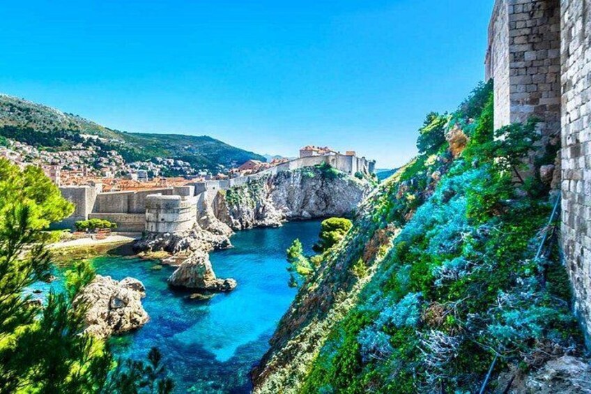 A coastal town with a clear blue sea, rocky cliffs, and a historic stone wall. 2