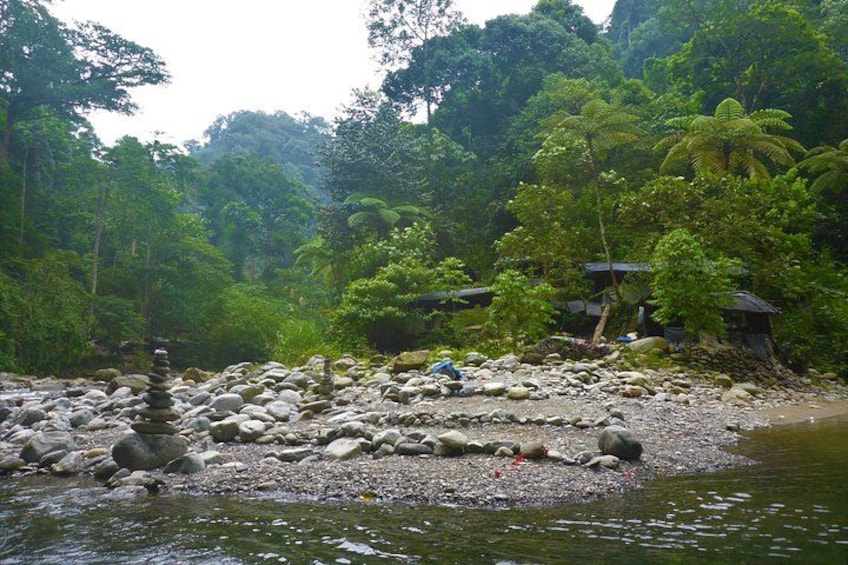 A riverbank with a stack of stones, lush greenery, and a small structure in the background. 2