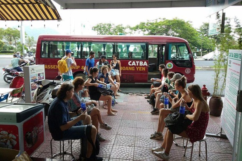 A group of people sitting on chairs under a bus with 'CATBA' and 'MOANG YEN' written on it. 5