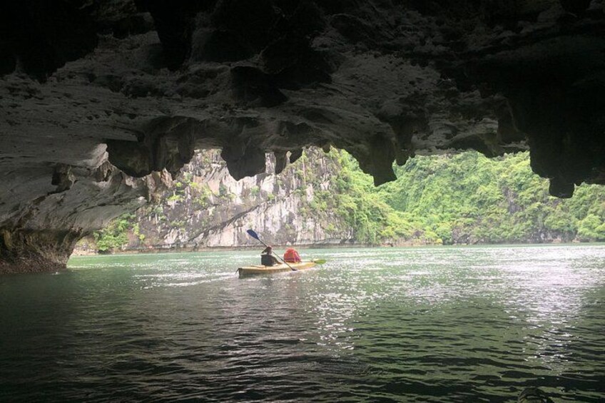 A person kayaking in a cave opening with water and greenery in the background. 3