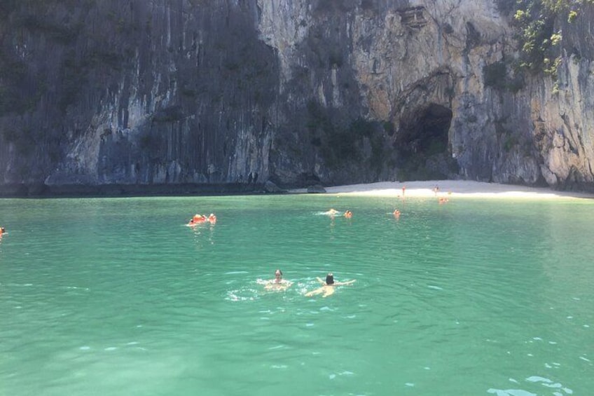 A beach with clear turquoise water, people swimming, and a rocky cliff in the background. 5