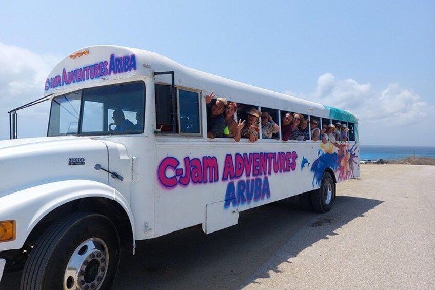 A white bus with colorful graphics and text advertising 'C-Jam Adventures Aruba' on its side. 4