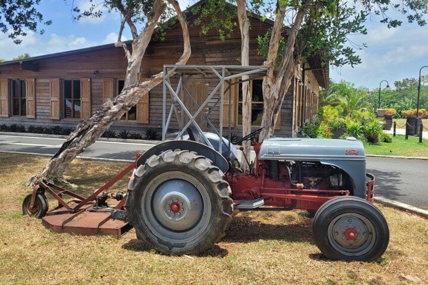 A vintage tractor parked in front of a wooden building with a tree leaning over it. 4
