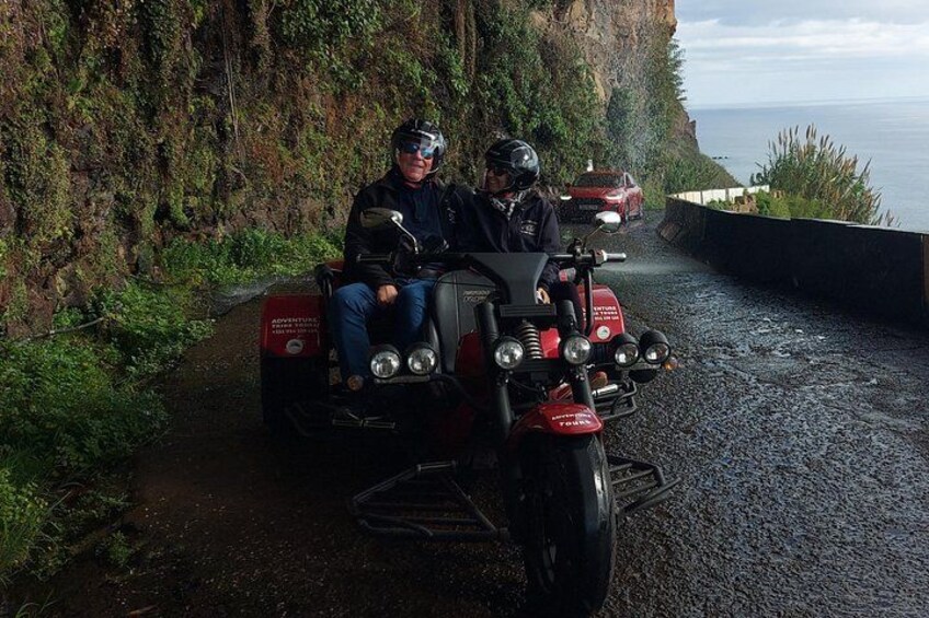 Een motor met twee bestuurders op een smalle weg met uitzicht op de oceaan en een klif. 1