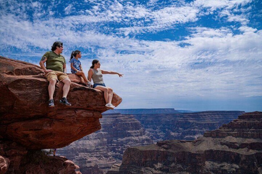 Three people sitting on a rock ledge overlooking a canyon. 3