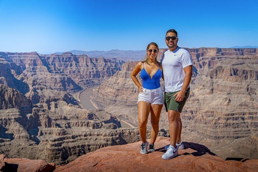 A couple standing on a rock with a canyon in the background. 1