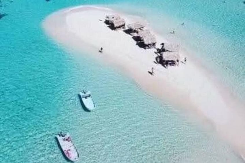 Una pequeña isla con una playa de arena blanca, rodeada de agua turquesa. Se ven dos embarcaciones en el agua. 5