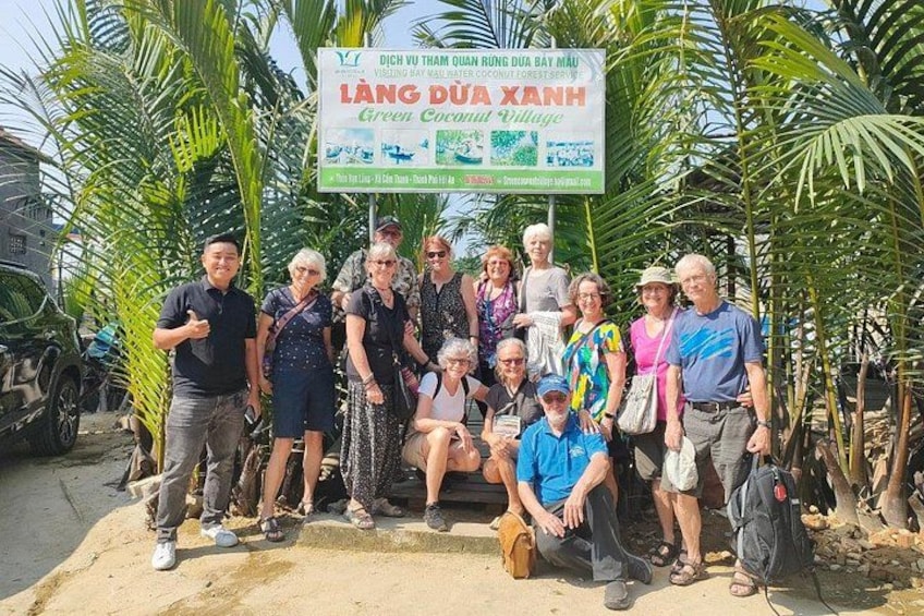 A group of people posing in front of a sign for Lang Dua Xanh Green Coconut Village. 2