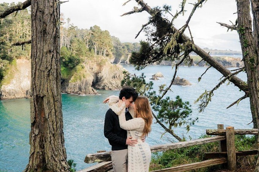 A couple embracing on a wooden bridge with a coastal landscape in the background. 1