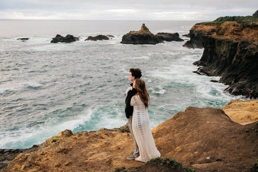 A couple standing on a rocky cliff overlooking the ocean. 3