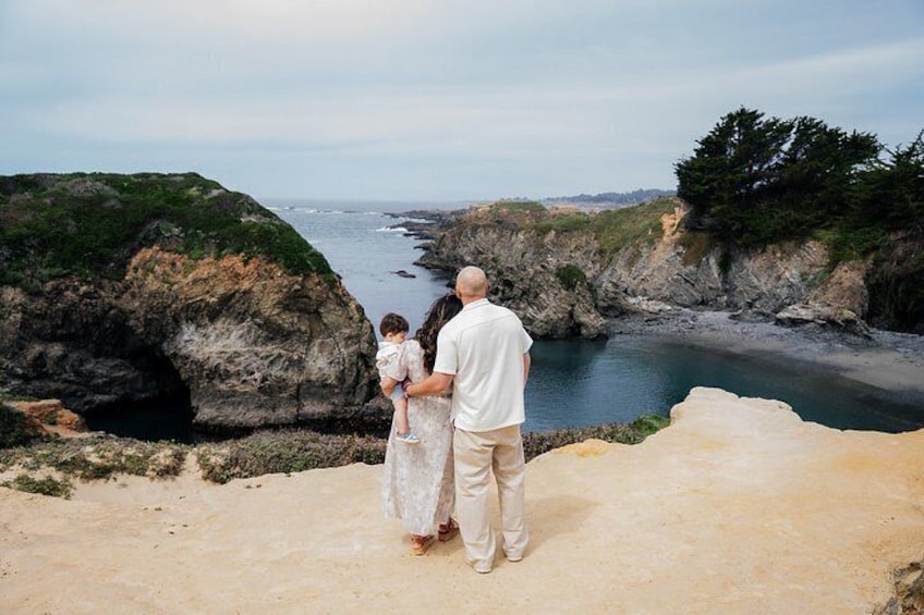 A man and a child standing on a sandy beach overlooking a rocky coastline with a body of water. 5