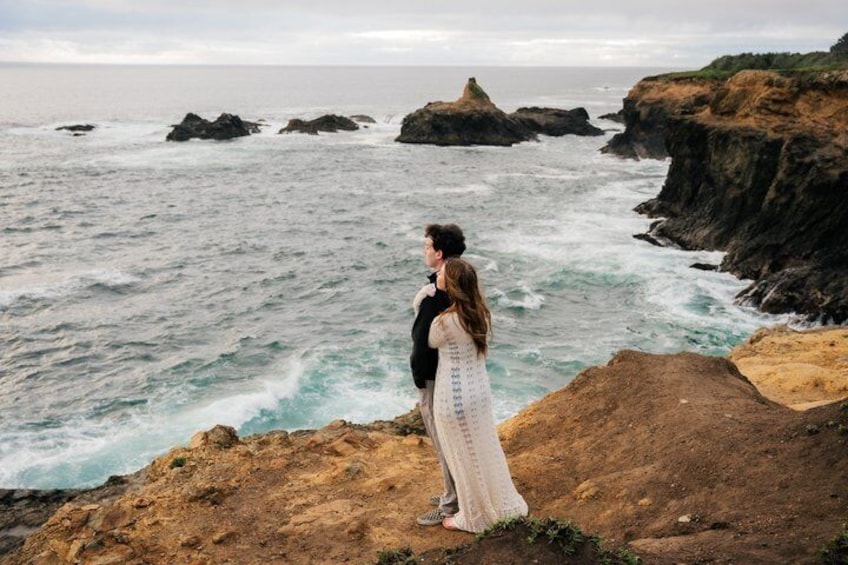 A couple standing on a rocky cliff overlooking the ocean. 3