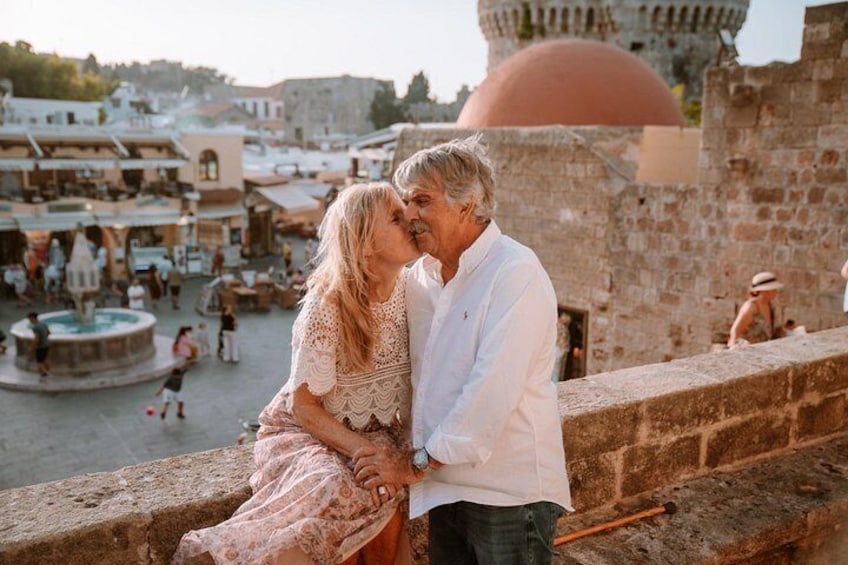A couple embracing on a stone wall overlooking a historic town with a prominent dome and a fountain in the background. 3
