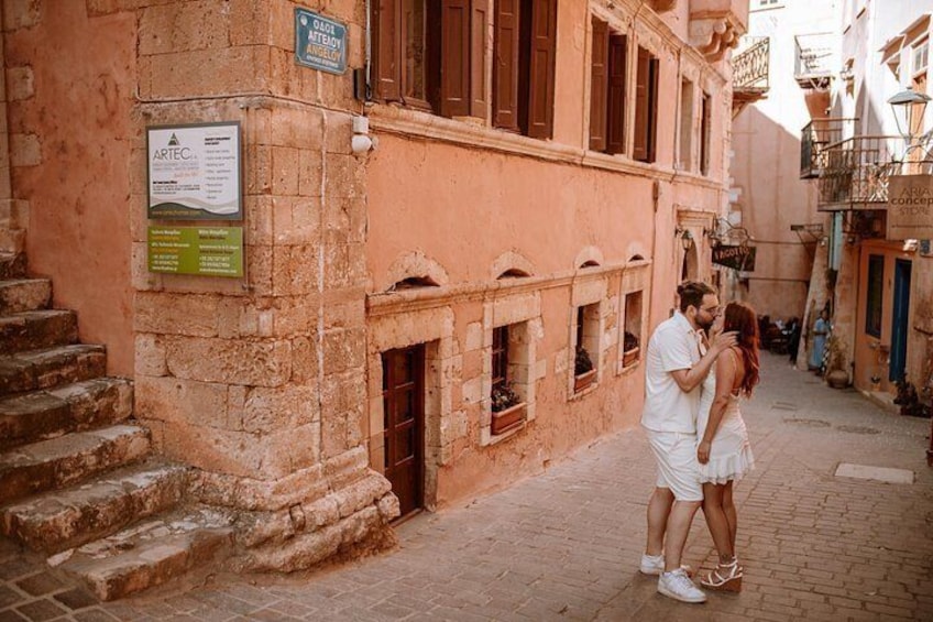 A couple embracing in a narrow street with stone buildings, a signboard, and a staircase. 4