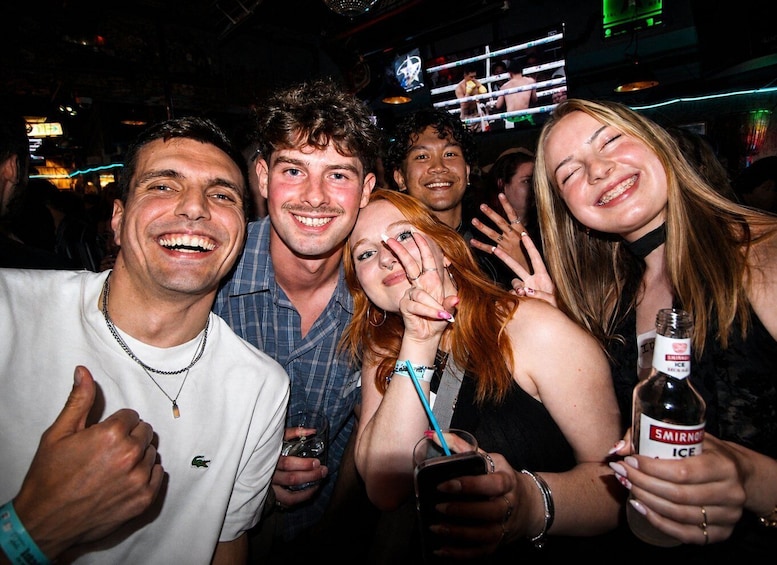 A group of people at a social event, some holding drinks and one with a thumbs-up gesture. 5