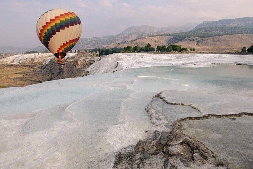 A hot air balloon over a geothermal area with mineral deposits and mountains in the background. 4