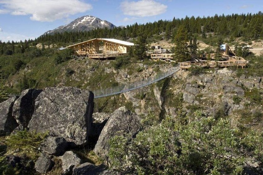 A mountain lodge with wooden structures, a suspension bridge, and a snow-capped peak in the background. 3