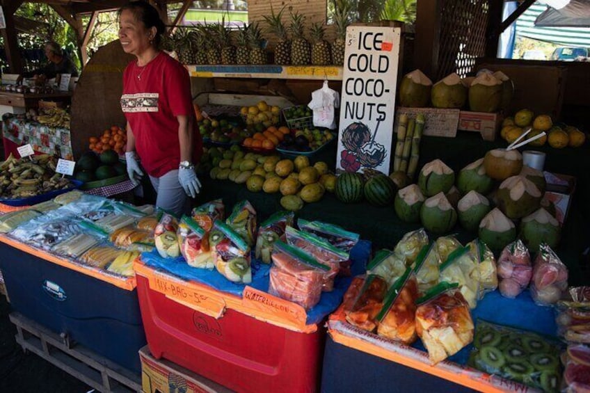 A market stall with a sign reading "ICE COLD COCO-NUTS" and various fruits and vegetables on display. 5