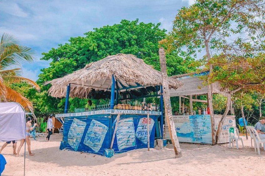 A beachside bar with a thatched roof, blue awning, and various signs. 2