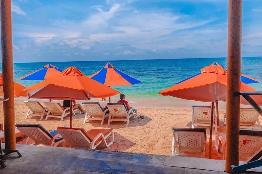 A beach with orange and blue umbrellas, white lounge chairs, and a clear blue ocean. 5