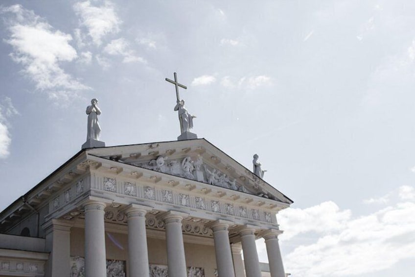 A neoclassical building with columns and statues, including a cross on top. 4