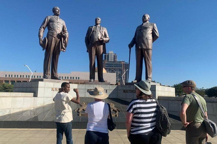 A group of people standing in front of a statue of a man holding a cane. 4