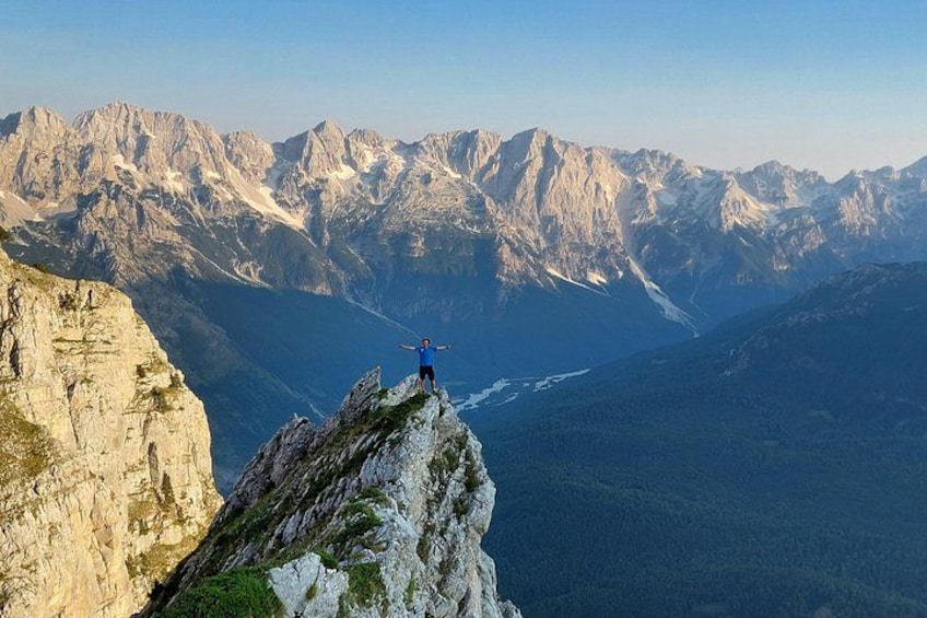 A person standing on a mountain peak with a rope, overlooking a valley with mountains in the background. 1