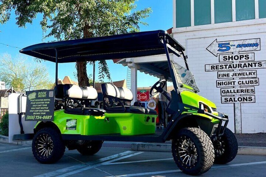 Un carrito de golf verde estacionado frente a un edificio con un letrero que enumera servicios como tiendas, restaurantes y galerías. 4