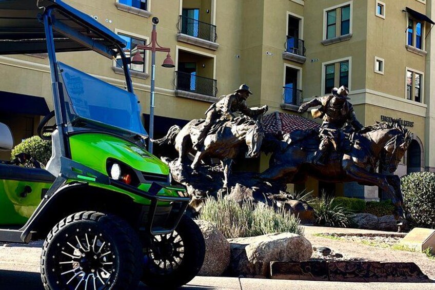 A green golf cart in front of a statue of a cowboy on a horse. 4