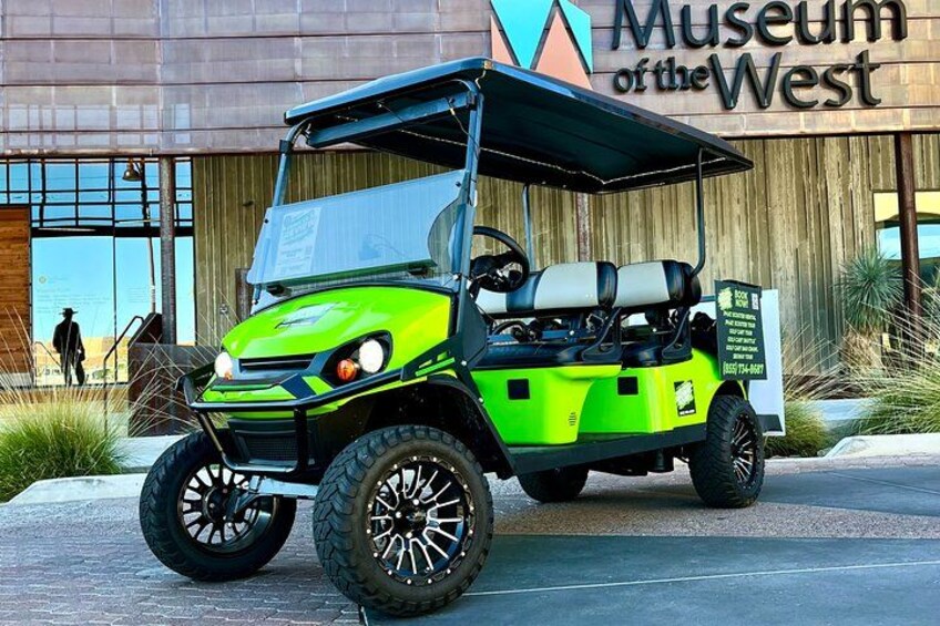 A green golf cart parked in front of the Museum of the West. 2