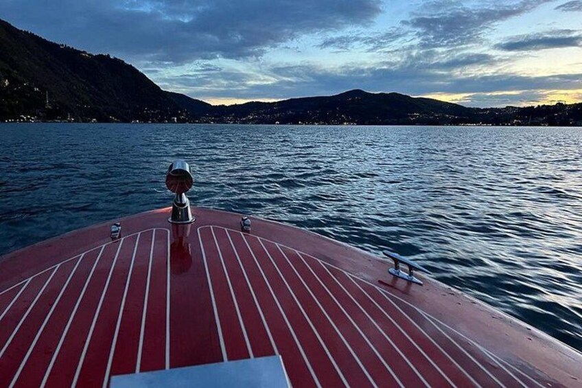 A boat's deck with a red and white striped pattern, a steering wheel, and a view of a calm lake with mountains in the background. 2