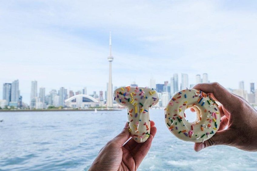 Two hands holding donuts with sprinkles in front of a city skyline with a tower. 2