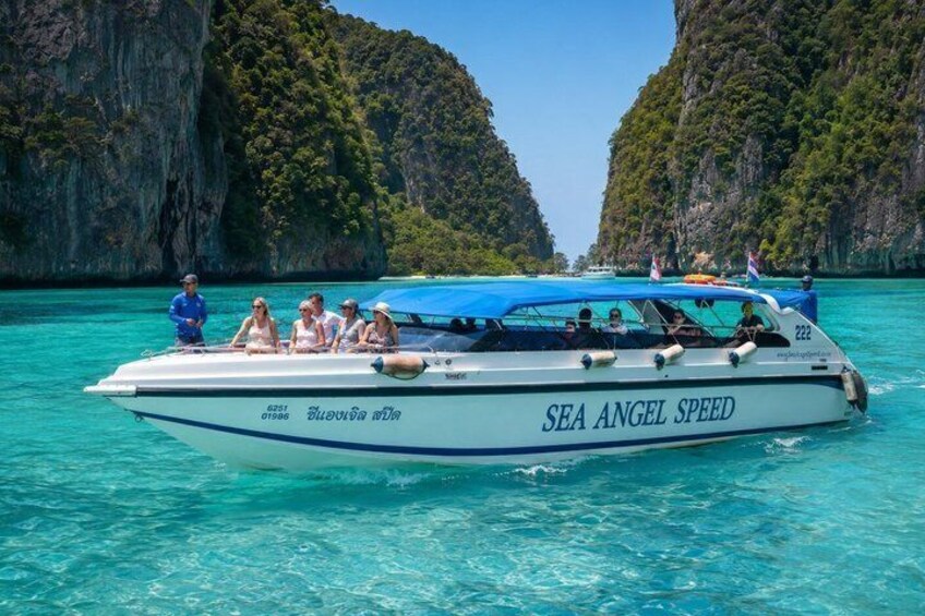 A boat named 'SEA ANGEL SPEED' with passengers on a turquoise sea, surrounded by lush green cliffs. 1