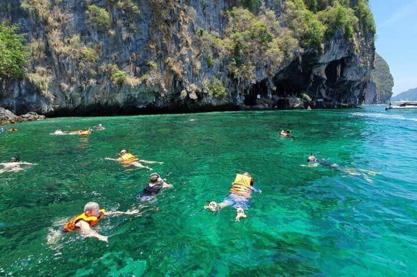 People swimming in clear turquoise water near a rocky cliff. 3